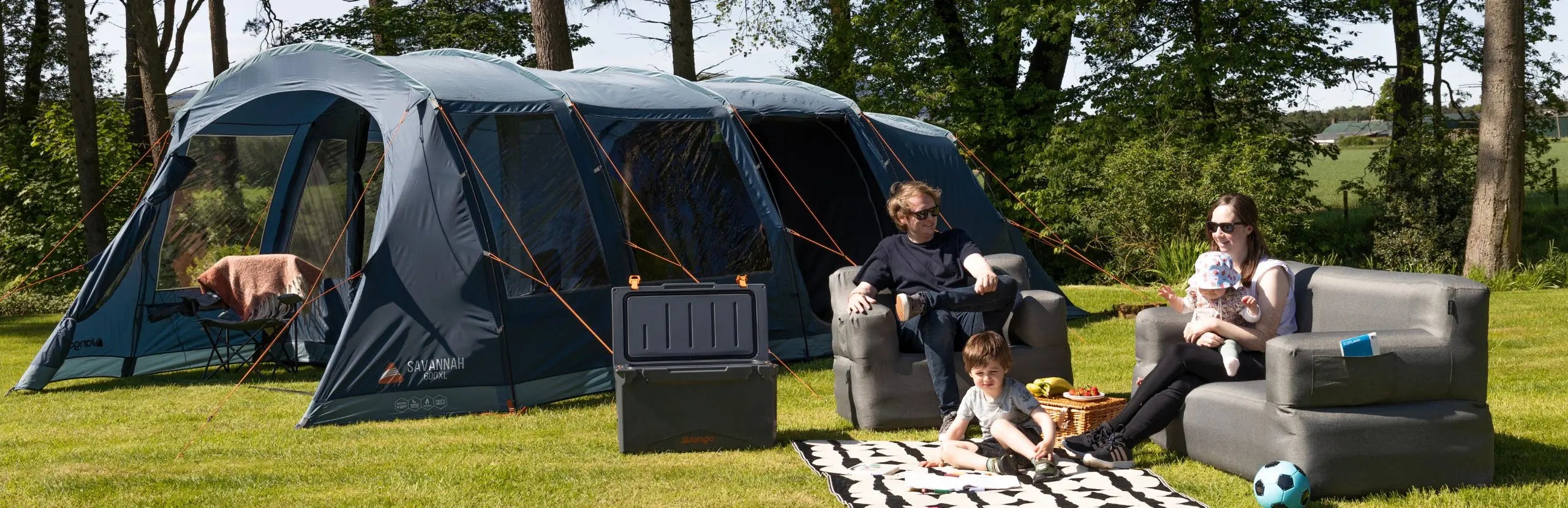 Family camping outdoors with a large Vango Savannah 600xl POled tent and outdoor furniture.