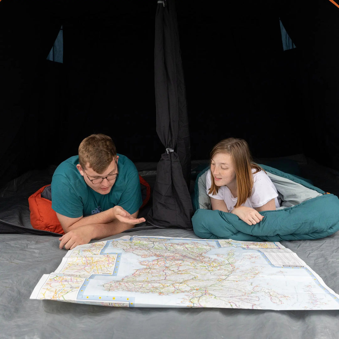 Close-up of two campers inside the Vango Savannah Air 400 tent, lying on the sewn-in groundsheet and planning their route with a map—perfect for couples and small families.