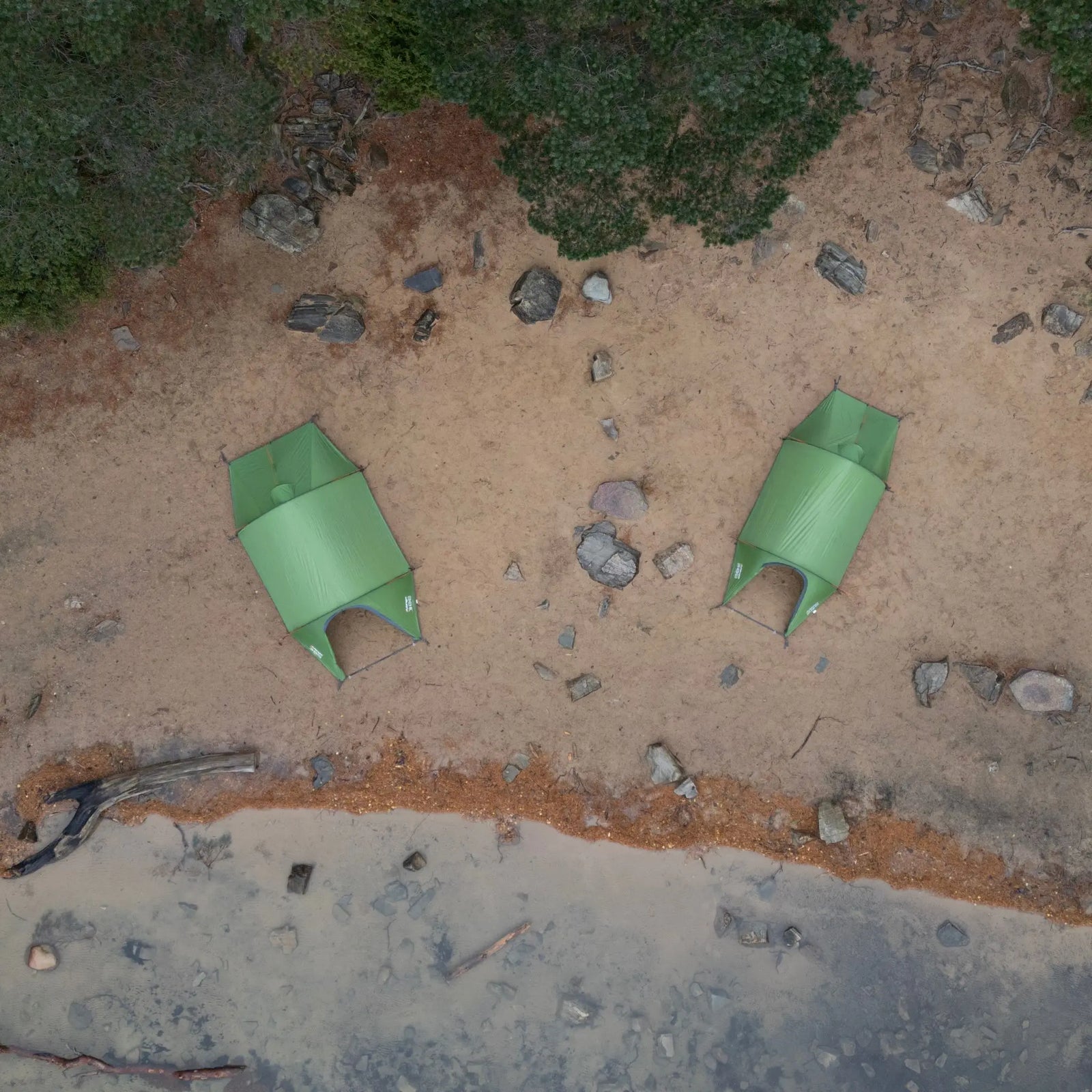 Aerial view of two Vango Scafell 200 2-man tents pitched on a sandy terrain by a lake, highlighting its compact and lightweight structure for trekking and backpacking adventures.