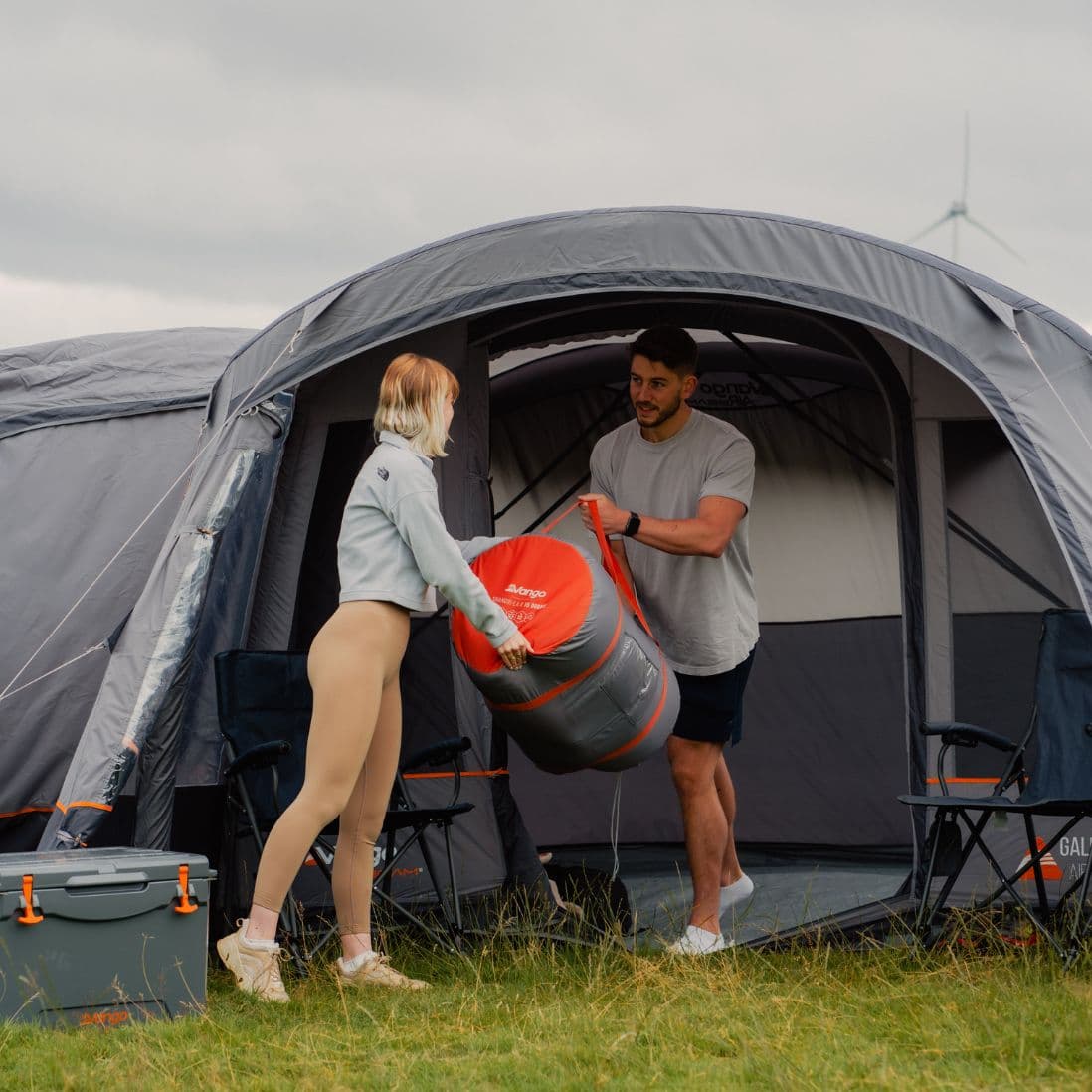 Man and woman carrying the packed Vango Shangri-La II 15cm Double self-inflating mat outside a tent, demonstrating its compact storage.