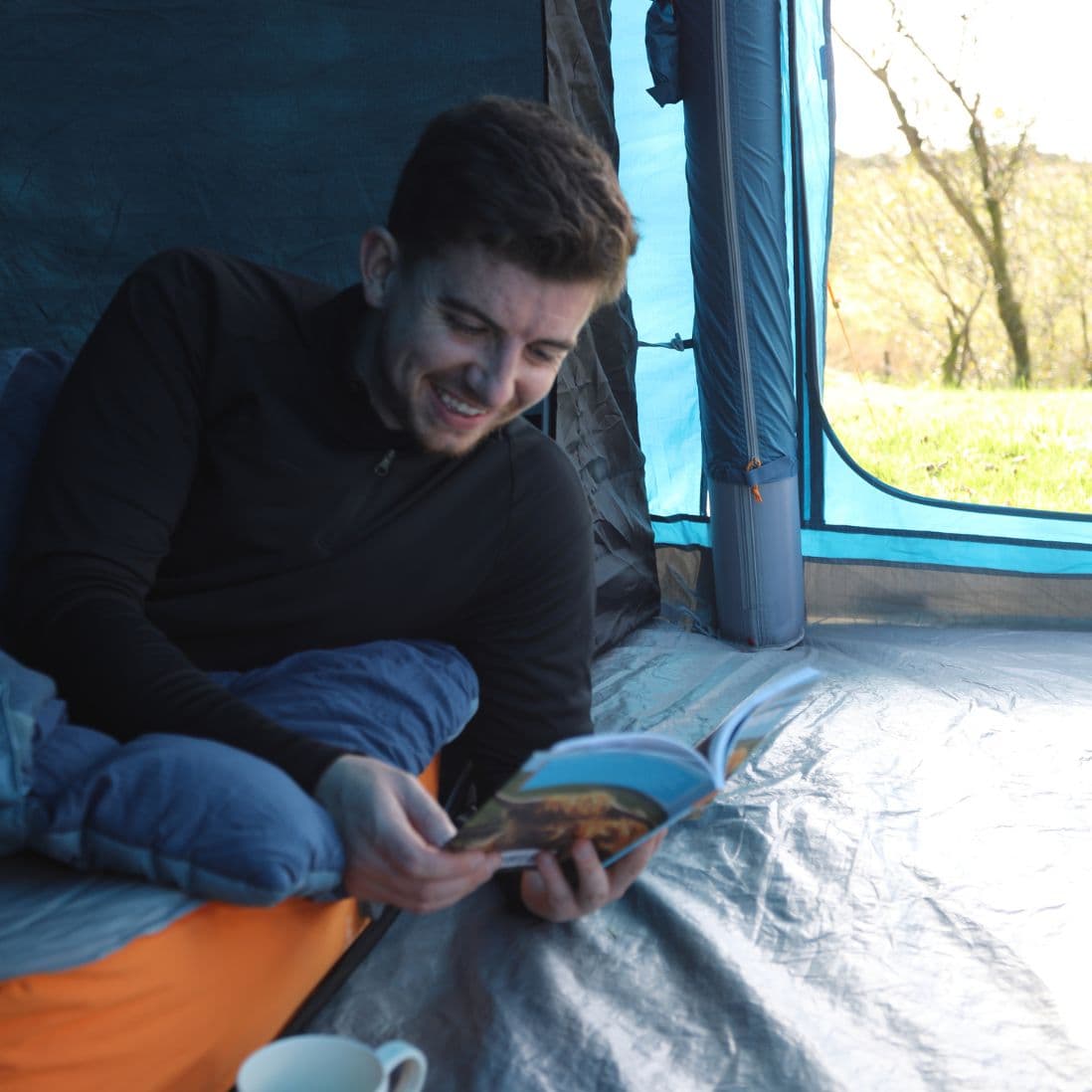 Man reading a book on the Vango Shangri-La II 15cm Double SIM in a tent, showing its comfort for camping trips.