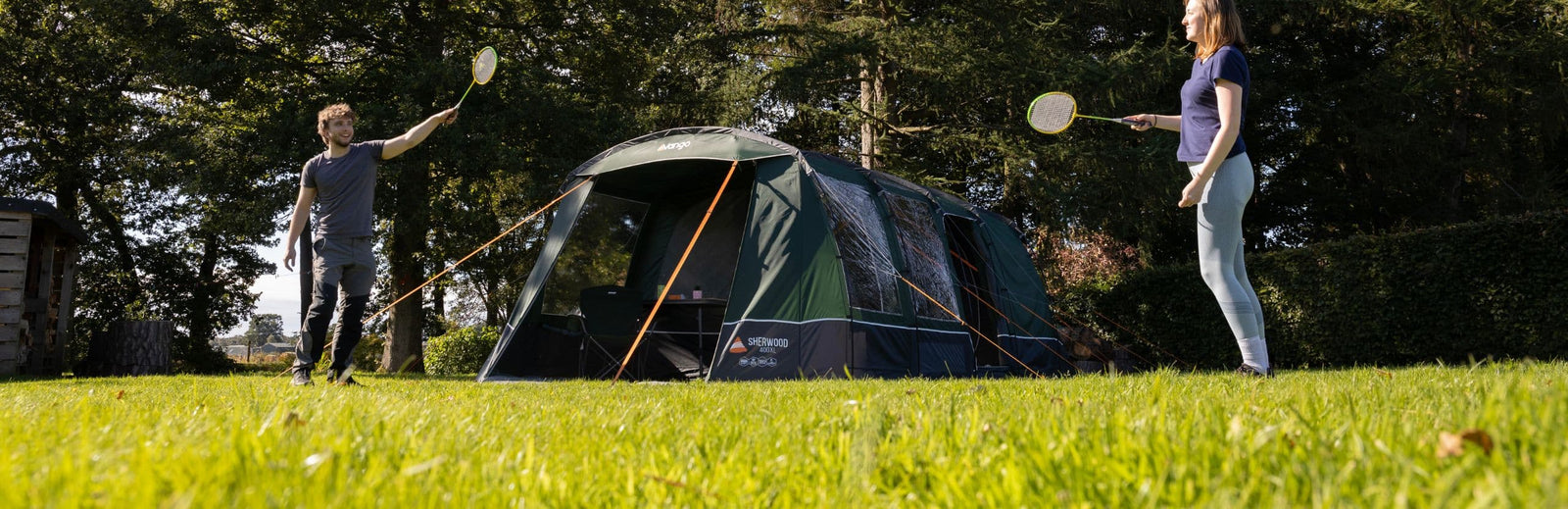 A couple playing badminton outside the Vango Sherwood 400XL Poled Tent, a 4-man tent, set up in a garden setting.