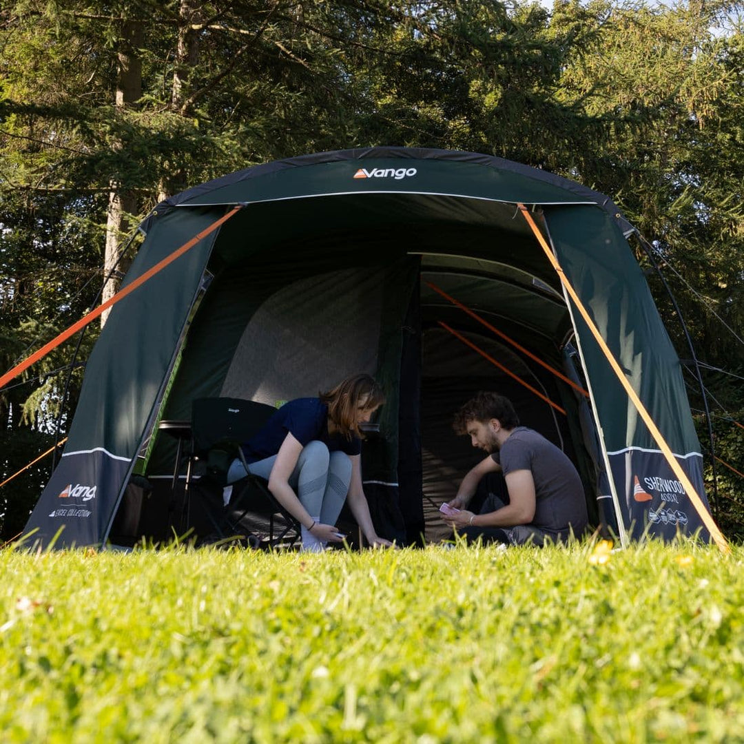 A couple enjoying their time inside the Vango Sherwood 400XL Poled Tent, showing its spacious front awning and living area.