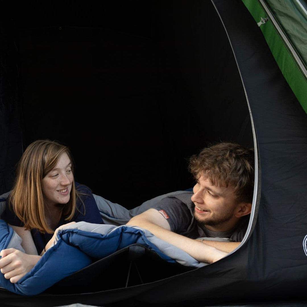 A couple enjoying their time inside the Vango Sherwood 400XL Poled Tent, showing its darkened bedroom area for comfort