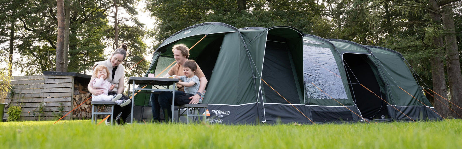 A family of four sitting around a table outside the Vango Sherwood 600XL Poled Tent, showcasing its spacious design and suitability as a 6 man family tent for outdoor camping trips.