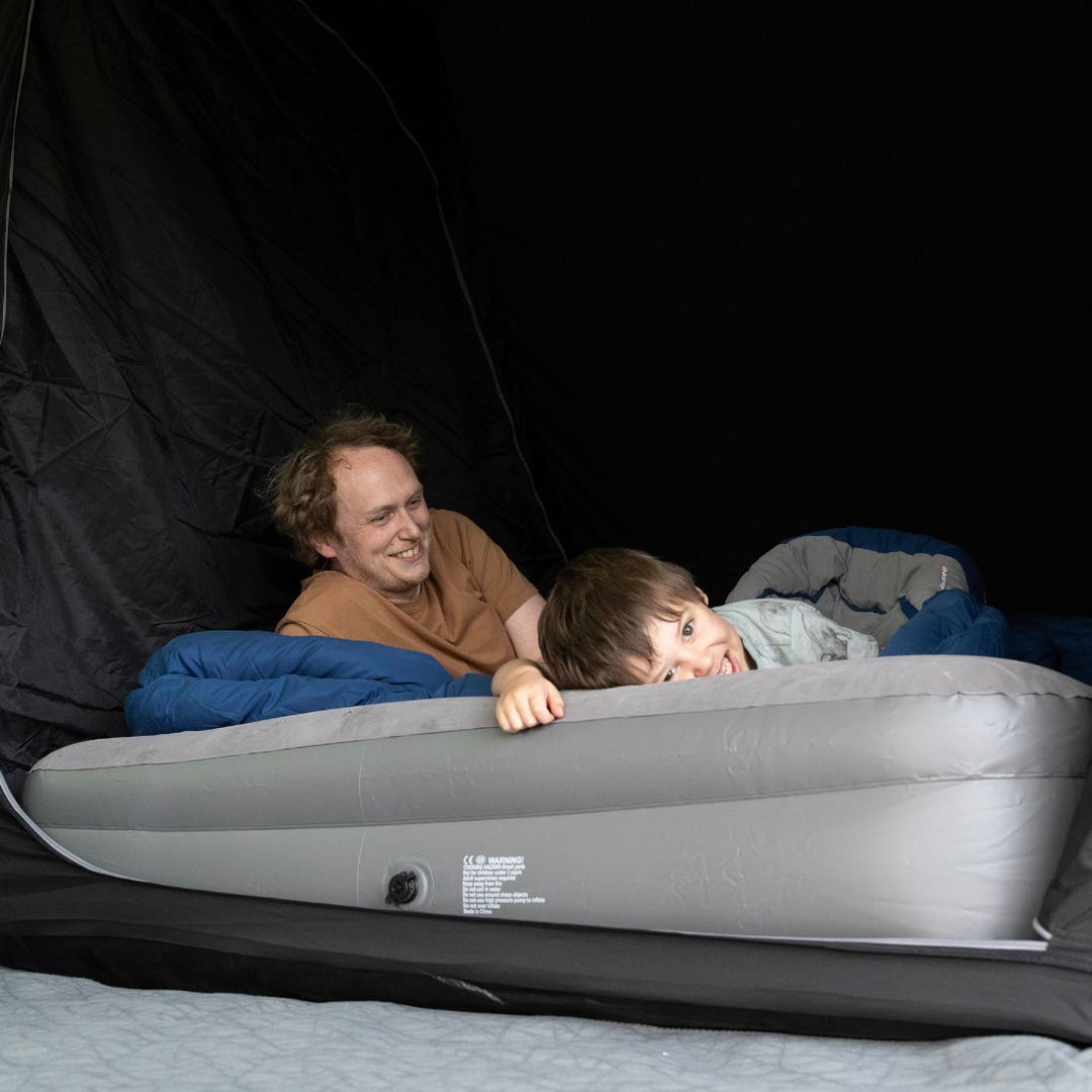 A father and son lying on an air mattress inside the midnight darkened sleeping area of the Vango Sherwood 600XL Poled Tent, highlighting its family-friendly features and sleeping capacity for six people.