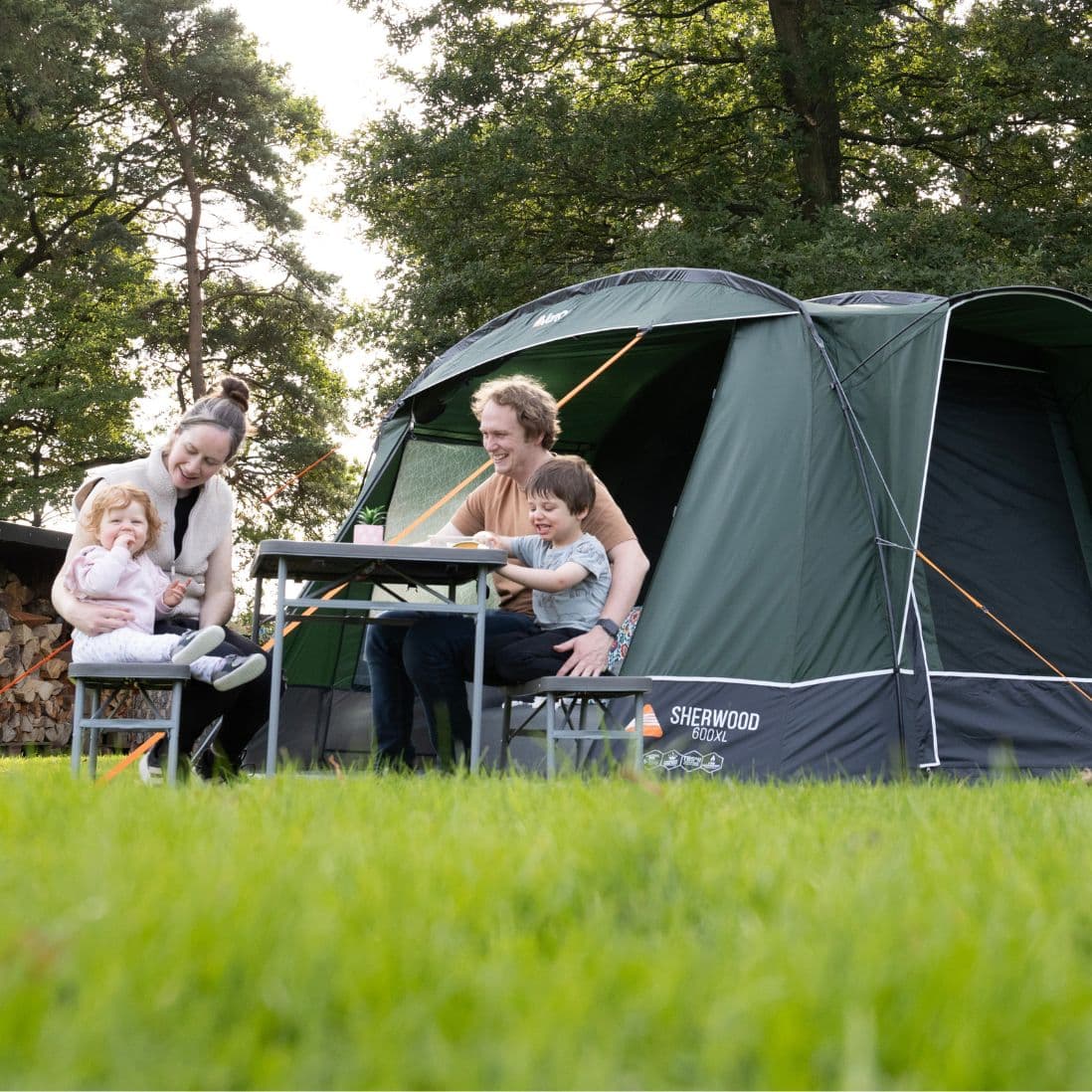 A family gathered for a meal in front of the Vango Sherwood 600XL Poled Tent, demonstrating its suitability as a spacious and versatile family tent for six people.