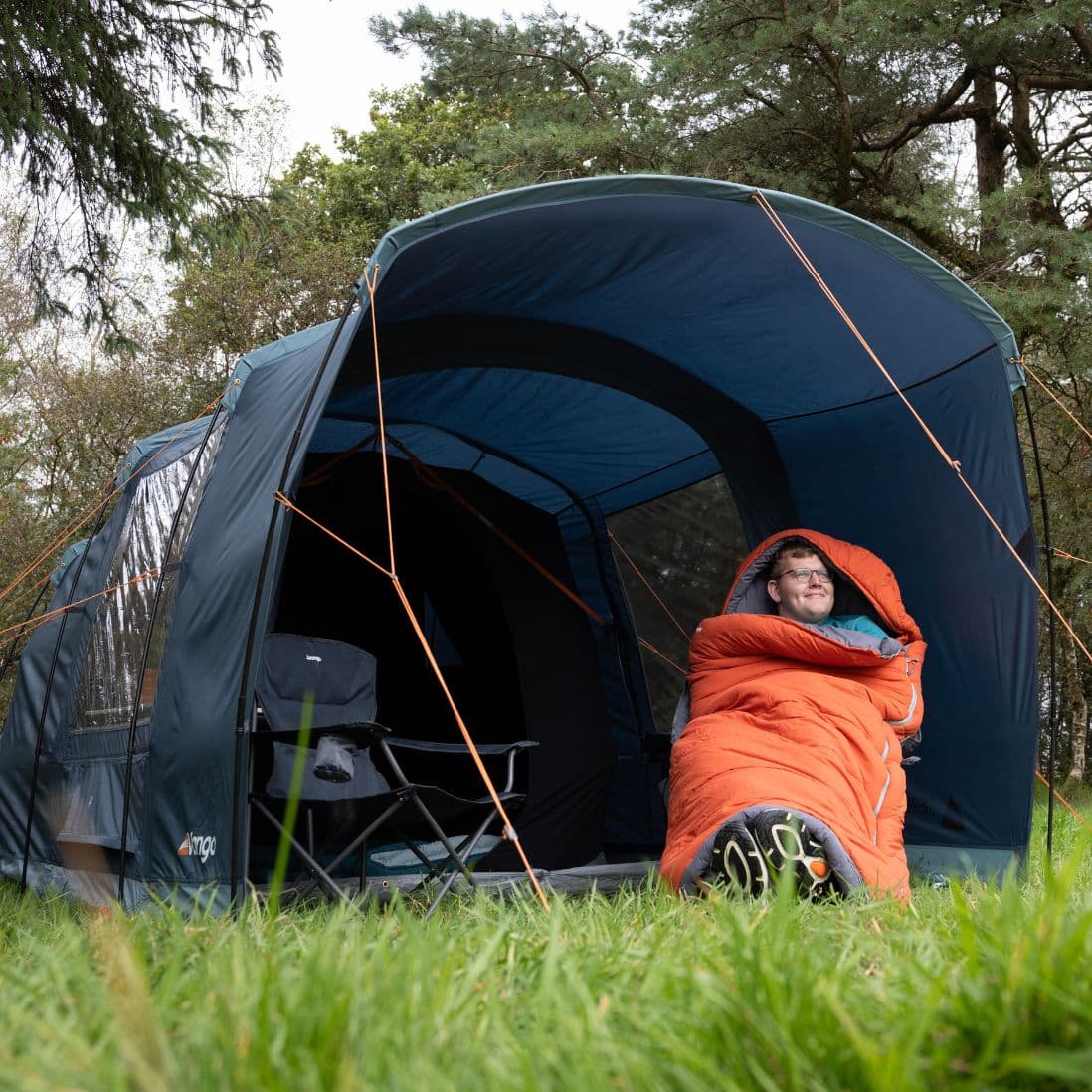 Image of a camper sitting outside the Vango Sierra 300 Poled Tent, demonstrating its versatility and comfort, an excellent choice for a 3 man tent.