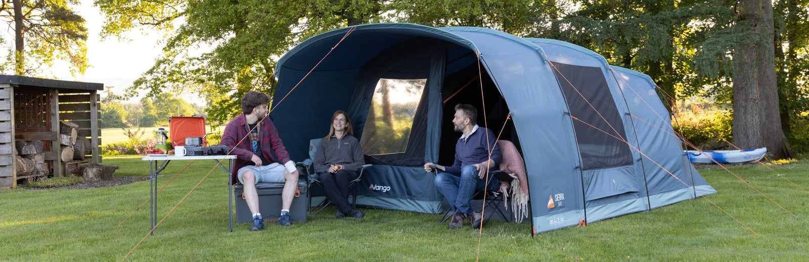 Family sitting outside the Vango Sierra 500 Poled tent, enjoying the campsite surrounded by greenery, with the tent showcasing its spacious entrance.