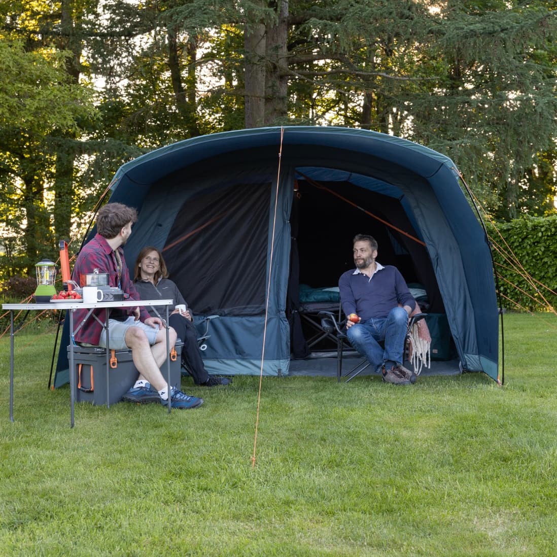 A family relaxing outside the Vango Sierra 500 Poled tent, with a view of its open entrance and sun canopy