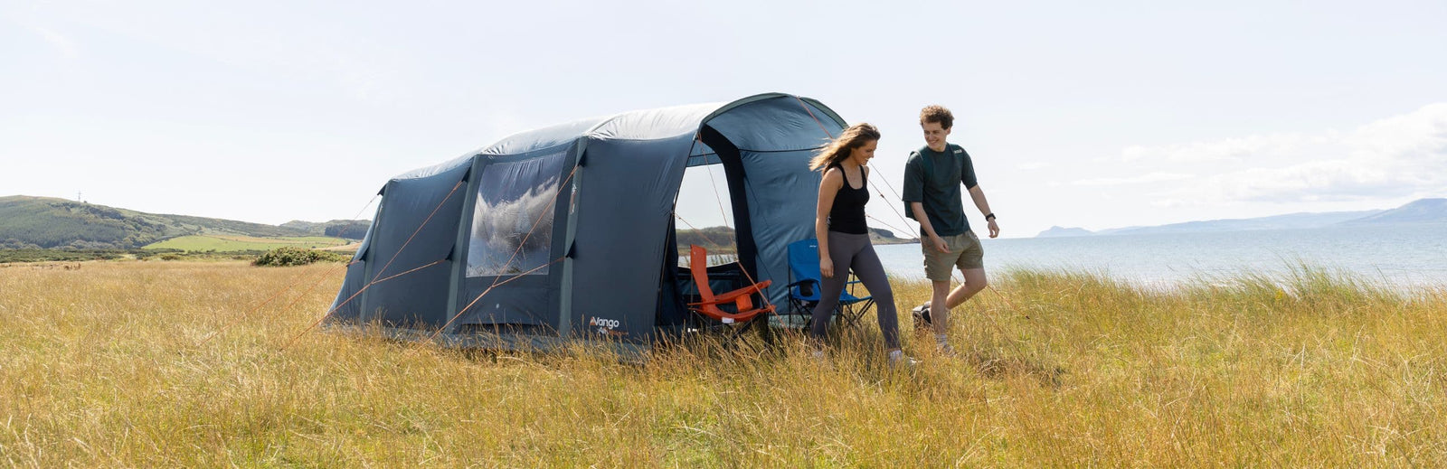 The Vango Sierra Air 300 3-man tent with campers walking beside it, highlighting its side entrance and large clear windows, perfect for couples.