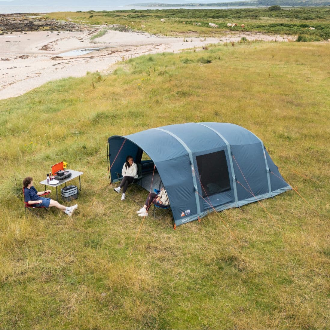 Overhead view of the Vango Sierra Air 500 AirBeam tent pitched on grassy terrain near a beach, with people sitting outside enjoying the open space.