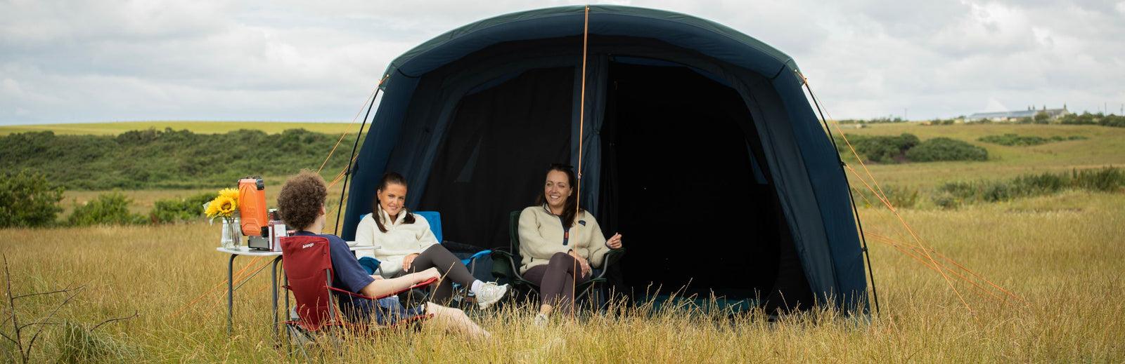 Front view of the Vango Sierra Air 500 AirBeam tent with its entrance open, showing three people sitting inside on camping chairs, relaxing and smiling.