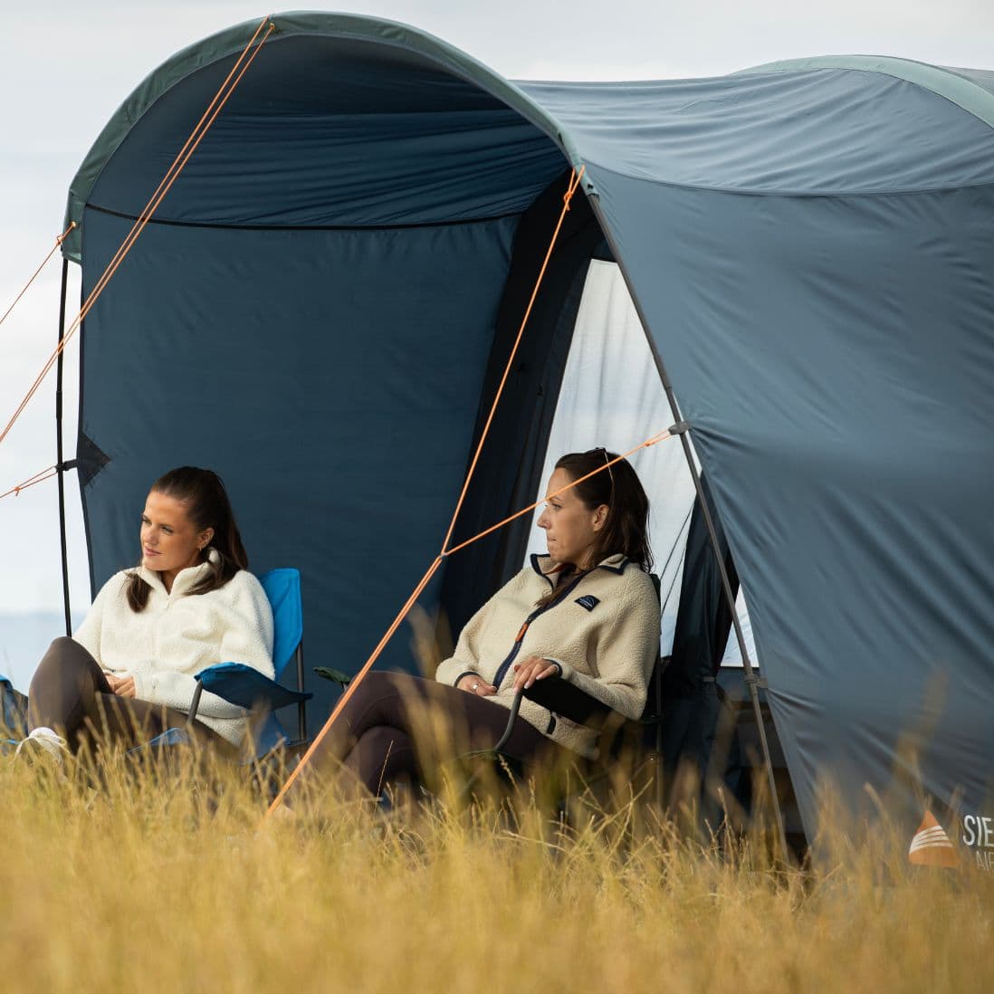 Side view of two people sitting under the pre-attached canopy of the Vango Sierra Air 500 AirBeam tent, looking out at the surrounding countryside.