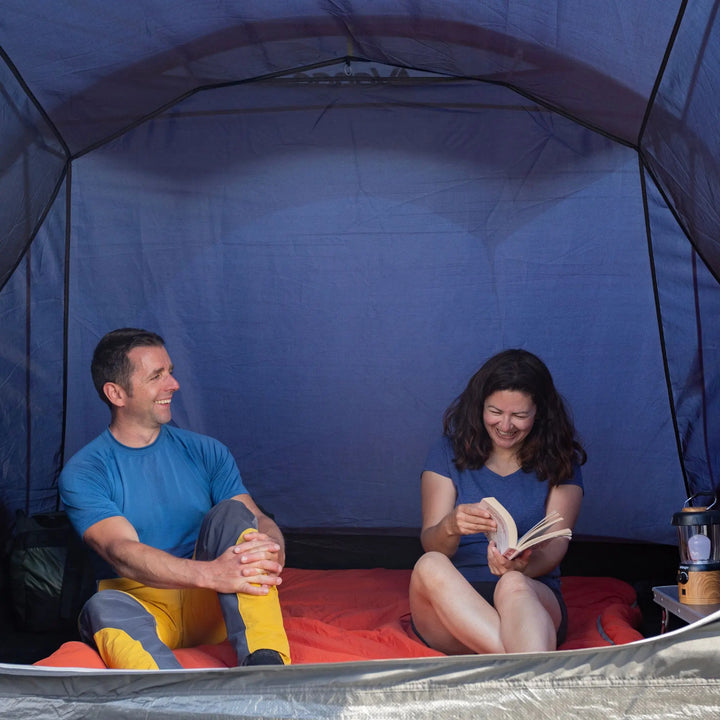 Two people inside a Vango Sorrento 600XL Tent, one reading a book.