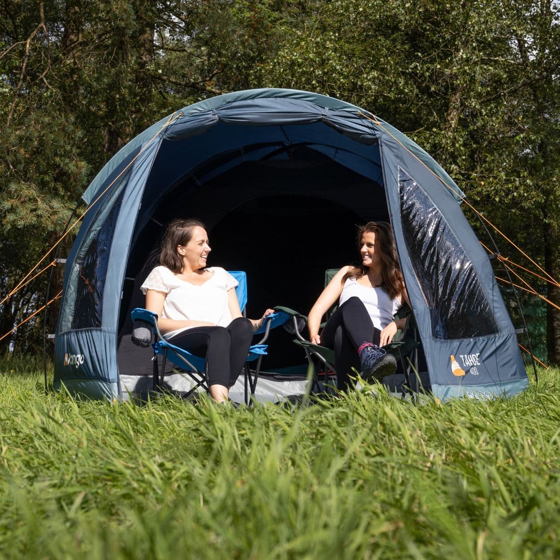 Two women relaxing at the entrance of the Vango Tahoe 400 4 man tent, surrounded by greenery.