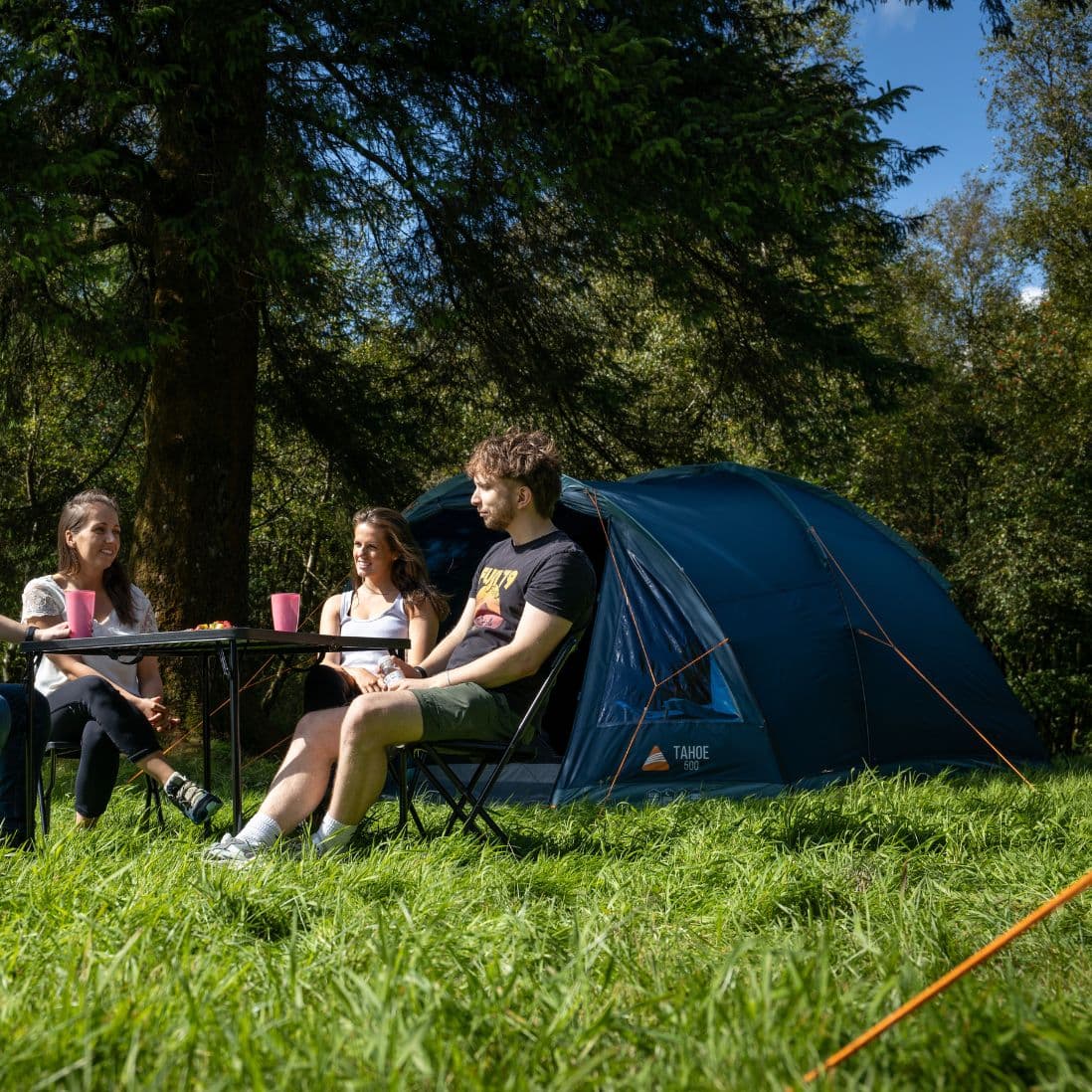 A group relaxing outside the Vango Tahoe 500 tent, showcasing its spacious design and suitability as a 5 man festival tent