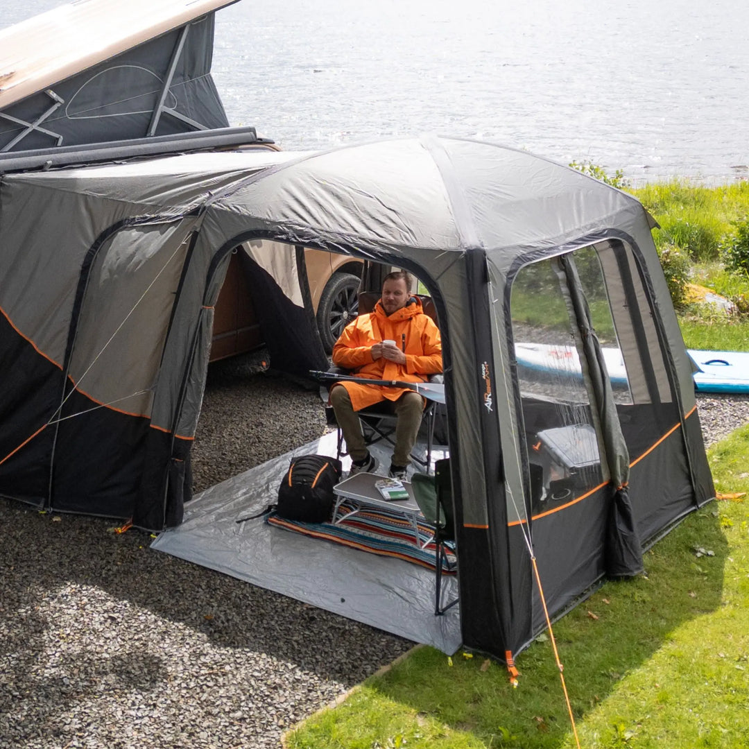Vango Tailgate AirHub II Low Drive Away Awning next to a lake attached to a VW campervan with its doors open. 