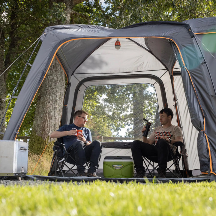 Outdoor setup of the Vango Tailgate Hub II Low awning, connected to a car with two campers enjoying their day.