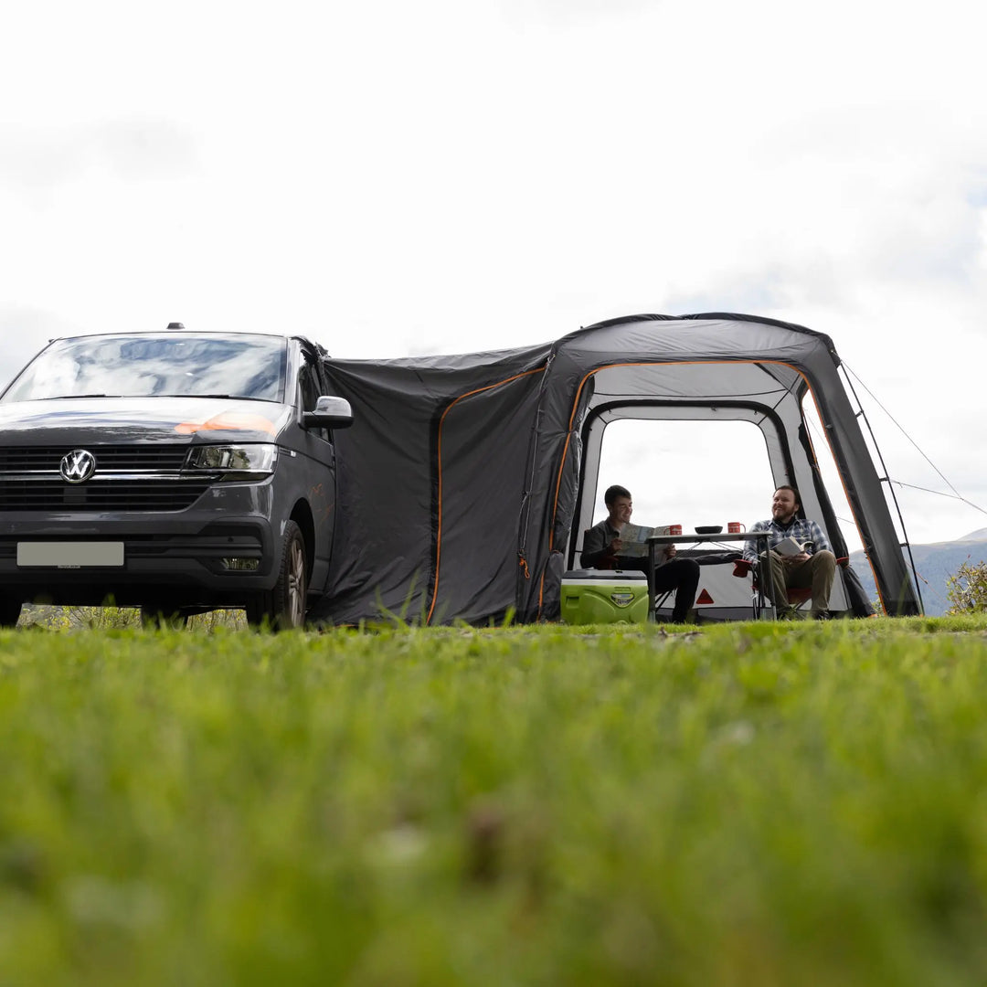 Interior view of the Vango Tailgate Hub II Low awning, with two people relaxing on camping chairs, highlighting the liveable space inside.