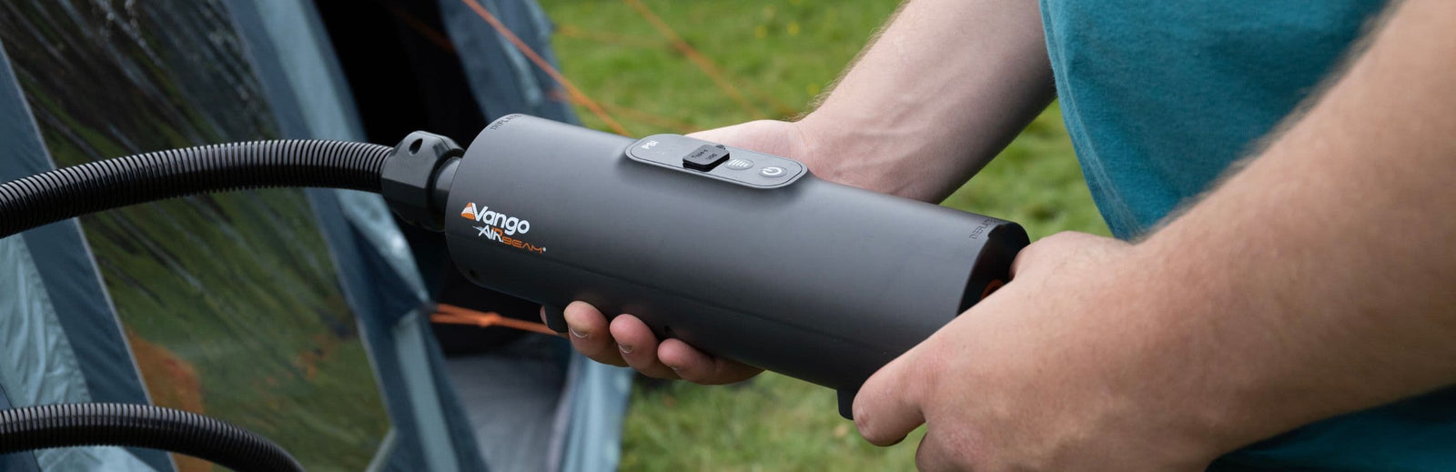 Close-up view of the Vango Tempest AirBeam Pump in use, with a coiled hose attached, held by a person outdoors near a tent.