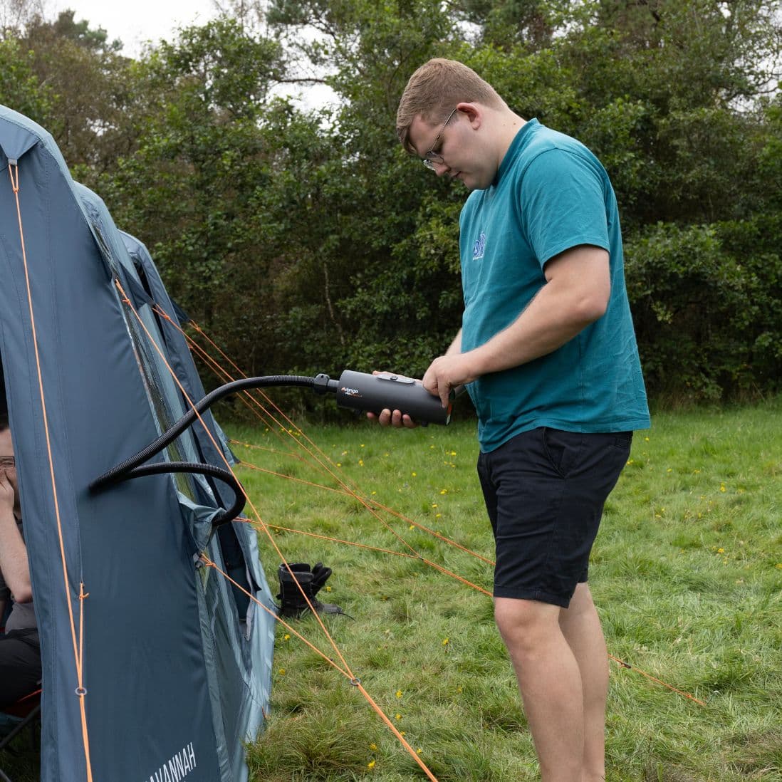 Person operating the Vango Tempest AirBeam Pump to inflate a tent, standing on grass in a camping setting.