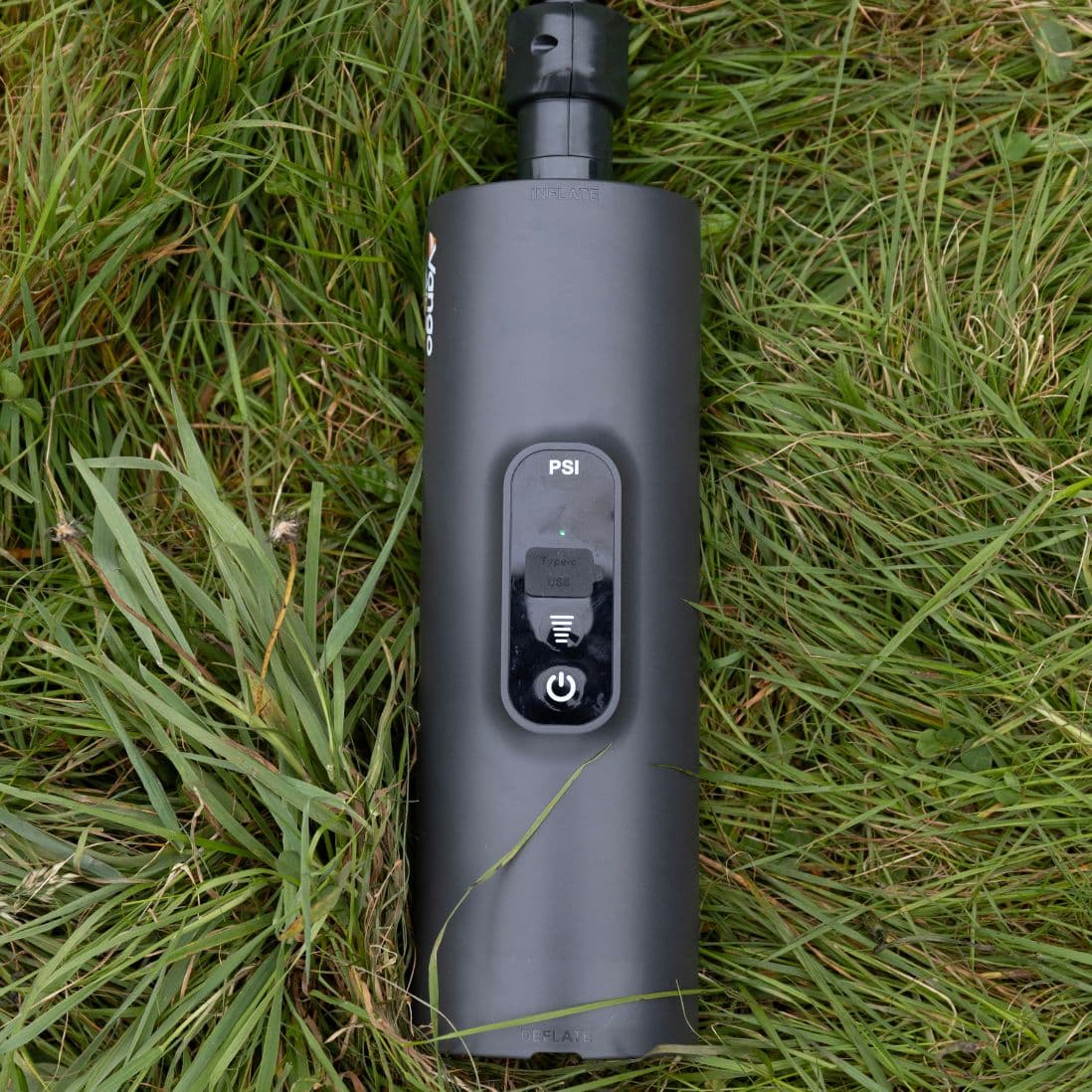 Vango Tempest AirBeam Pump placed on grass, showing its control panel with PSI display and power buttons.