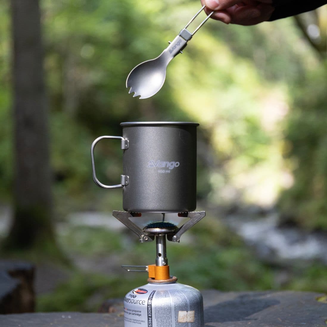 Vango Titanium Folding Spork held above a Vango gas stove with a camping mug. Compact, lightweight camping cutlery for hikers and campers.