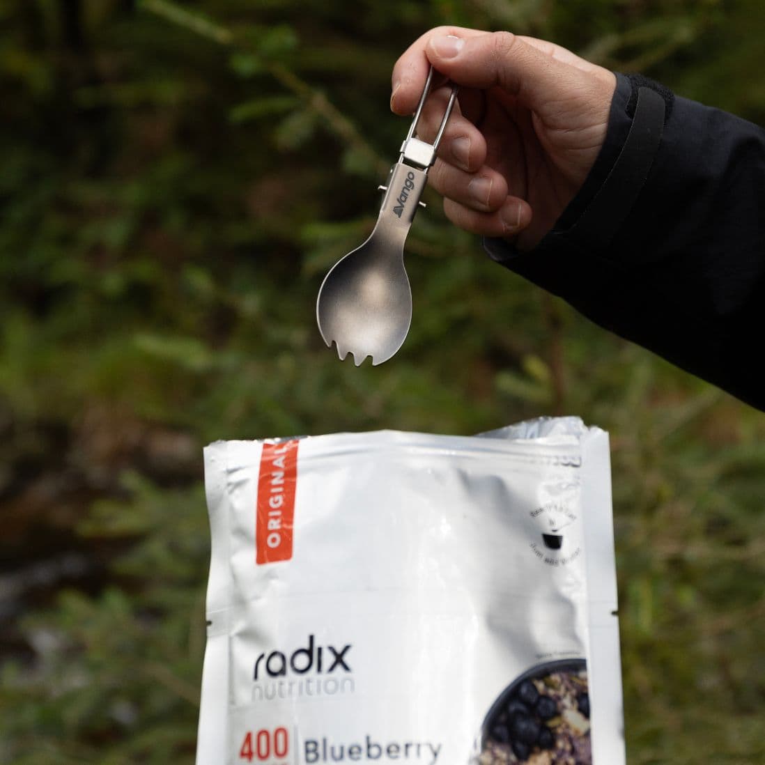 Vango Titanium Folding Spork held over a bag of camping food. Durable and lightweight camping utensil for outdoor meals.