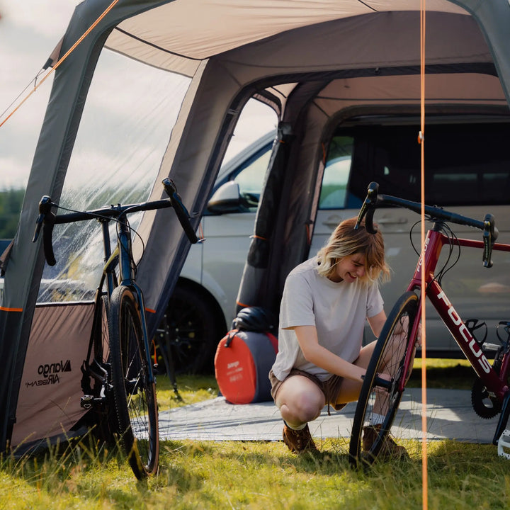 Cyclist adjusting a bike inside the Vango Versos Air Low, demonstrating its spacious interior and versatility for outdoor activities.