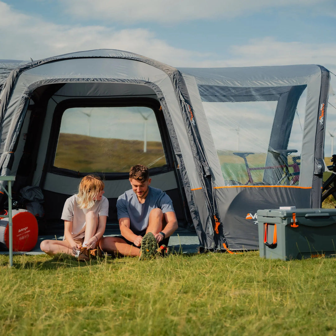 Couple relaxing at the side entrance of the Vango Versos Air Low Drive-Away Awning, enjoying the open living space and panoramic windows.