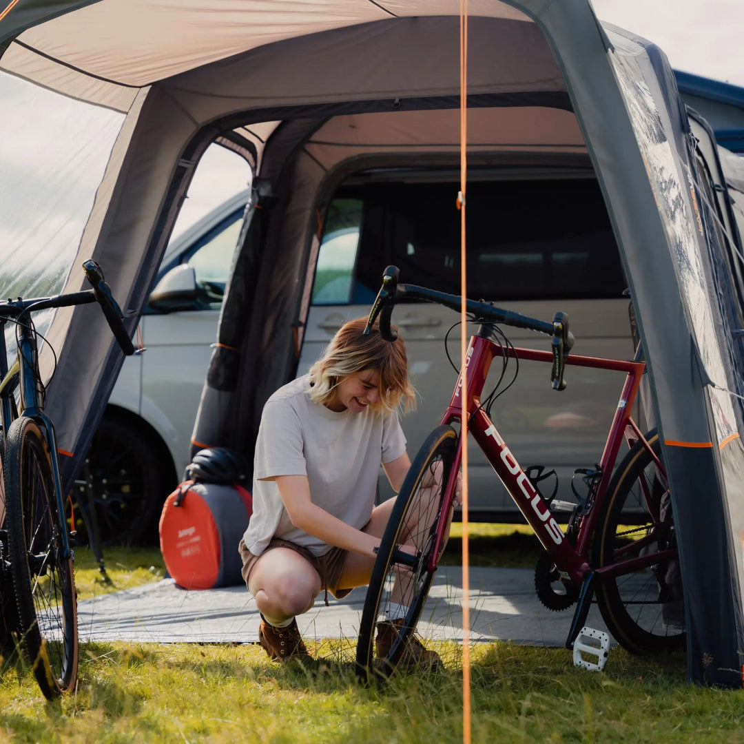 A cyclist adjusts a bike inside the Vango Versos Air Low campervan awning, which features a sewn-in groundsheet for added comfort and protection.