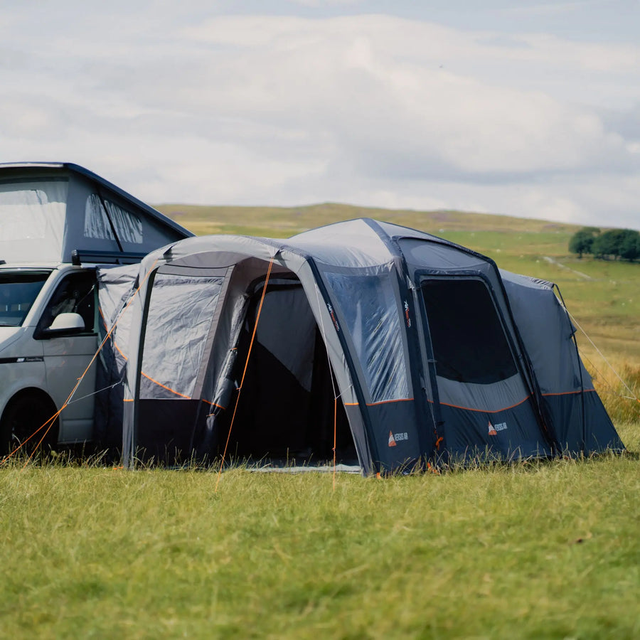 Vango Versos Air Low Drive-Away Awning attached to a VW campervan, pitched in a scenic grassy landscape with secure guy ropes.