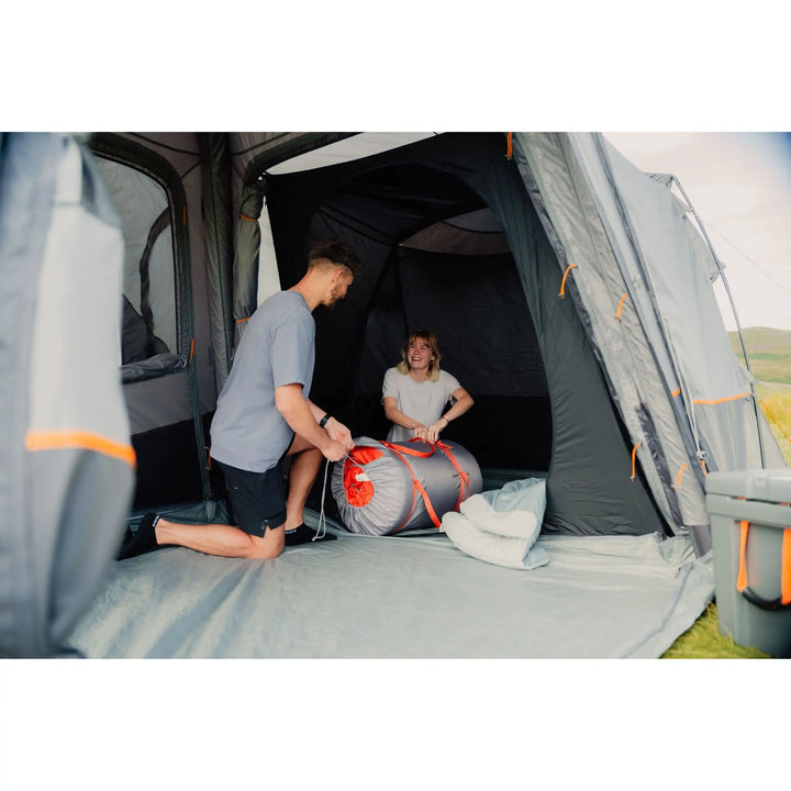 Couple setting up a Vango Versos Air Mid inflatable awning, rolling out a Vango Shangri La sleeping mat inside the spacious interior.