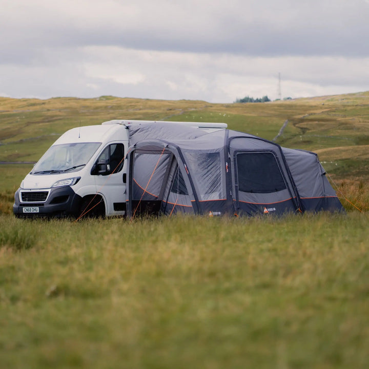 Vango Versos Air Mid inflatable awning set up beside a campervan in a grassy field, ideal for outdoor camping adventures.