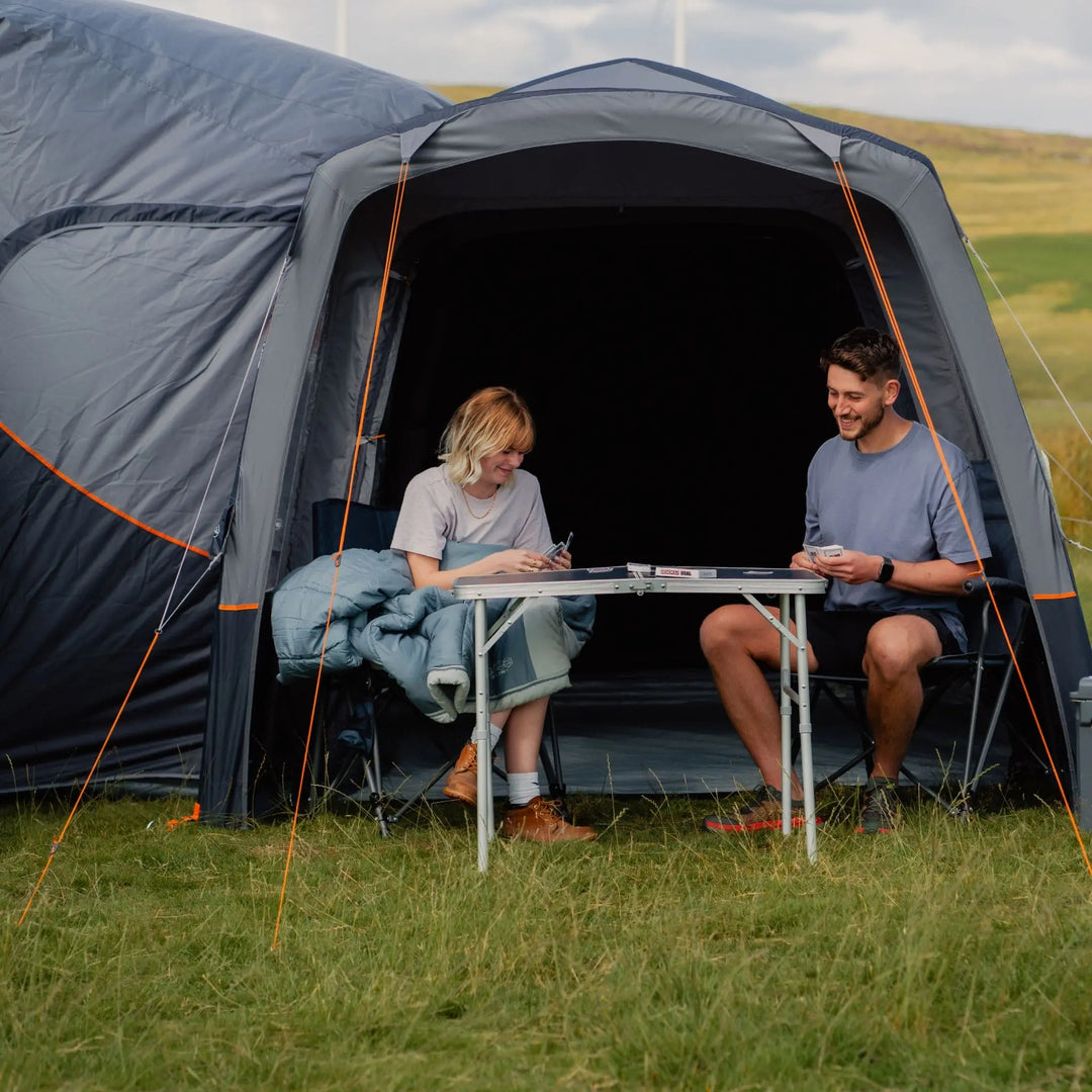 A couple sitting under the Vango Versos Air Mid awning built-in sun canopy, playing cards at a foldable camping table.