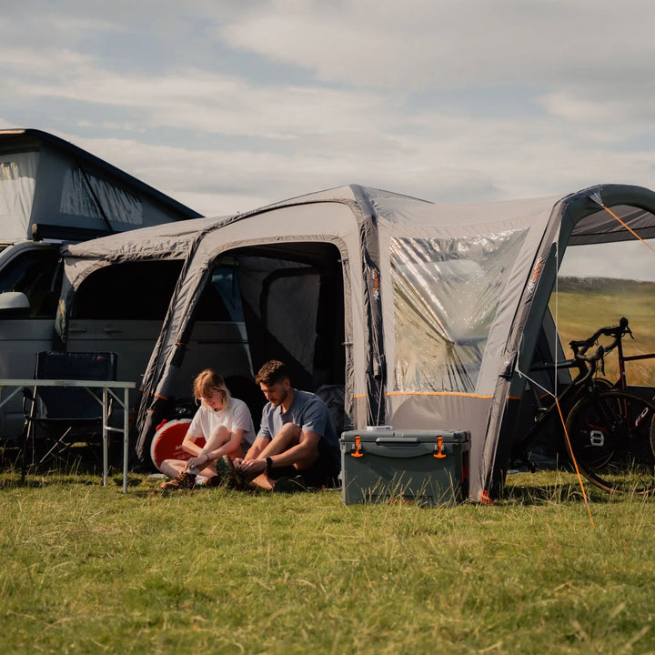 Outdoor setup of the VW campervan awning, with a couple relaxing at the side entrance, emphasising the awning’s comfort and shelter.