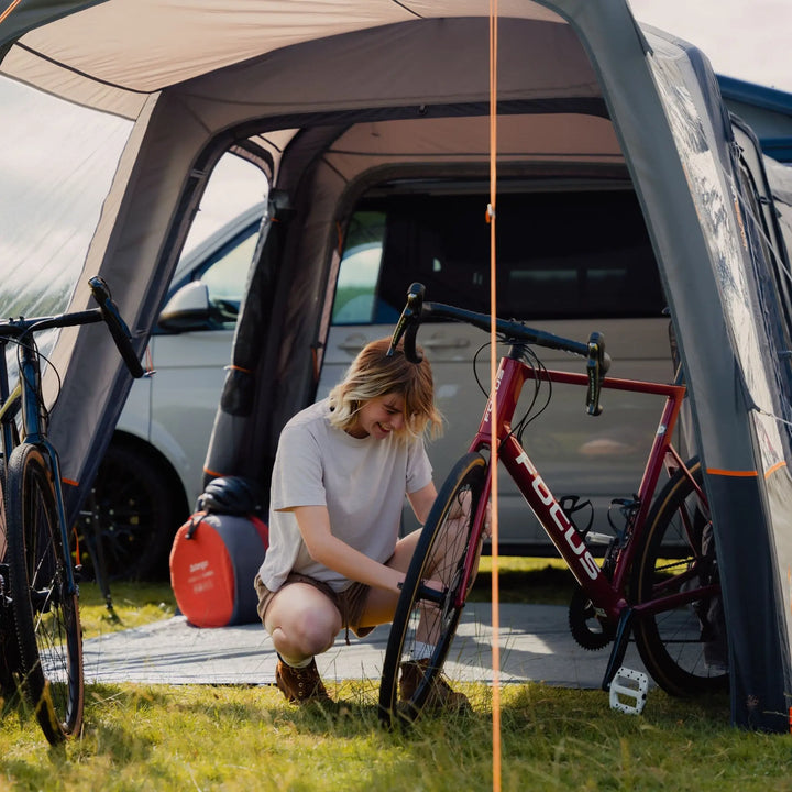 A cyclist adjusting their bike inside the Vango Versos Air Low campervan awning, demonstrating its practicality for active campers.