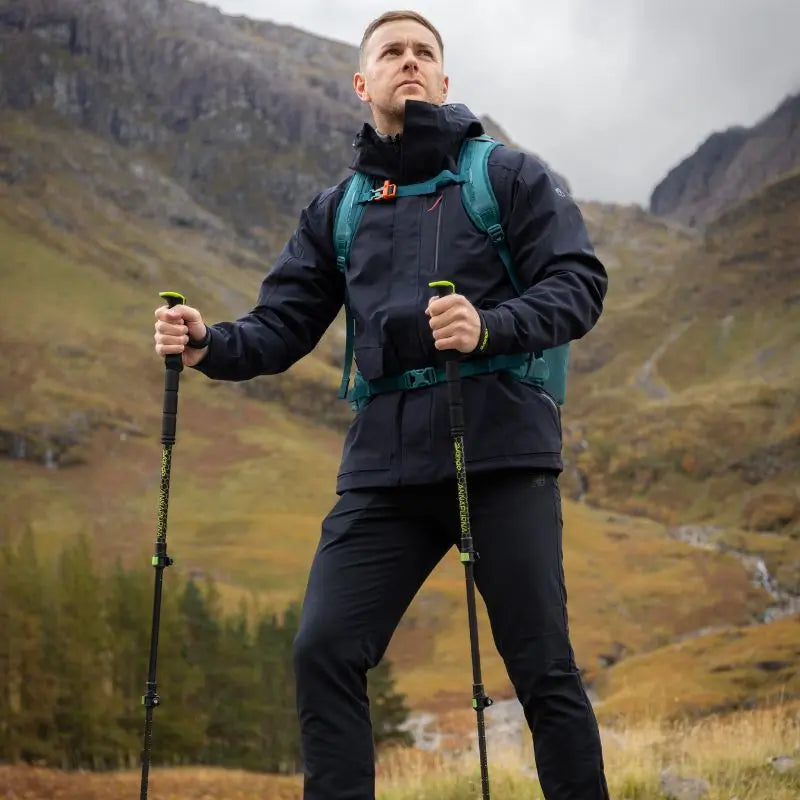 Man hiking in a mountainous area with trekking poles and a backpack.